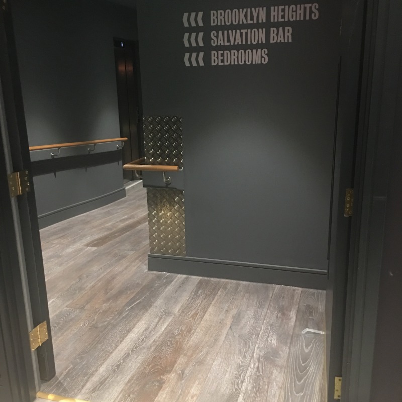 Ground Floor Corridor to Lifts - Corridor well lit & signposted. Doors open 180 Deg. Flooring smooth and flat. Slight incline down to lifts Wooden Bannisters either side.