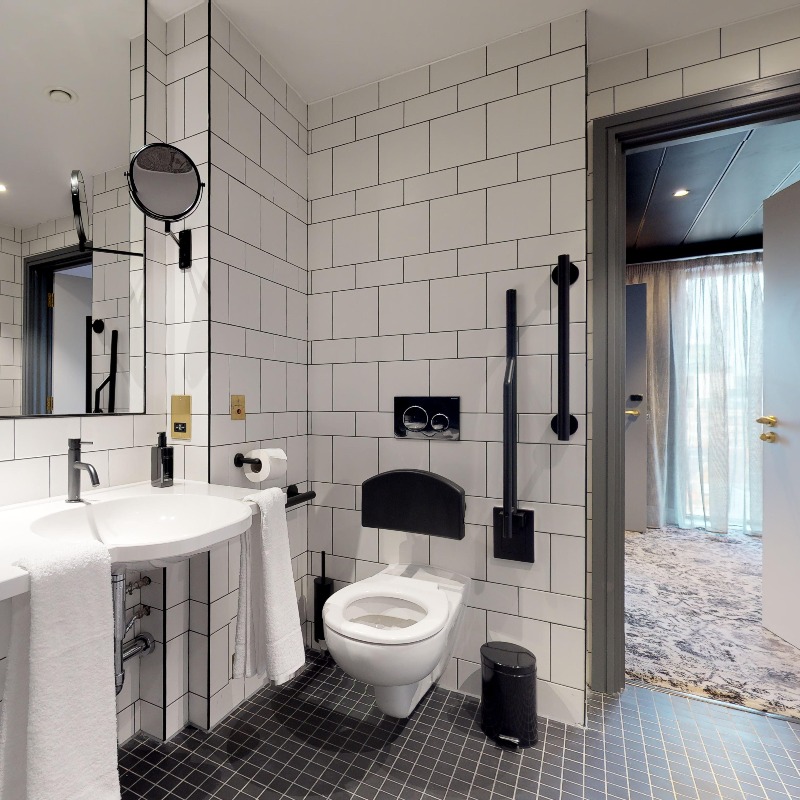 Liberty Wheelchair Access Room - WC - Black Backrest & 3 black grab rails at white toilet, 43cm high. Righthand transfer retracting rail. Shallow sink wheelchair height & 2 integrated rails. Within reach of toilet. Black lever tap. Emergency button on wall & floor. Shower wheelchair available.